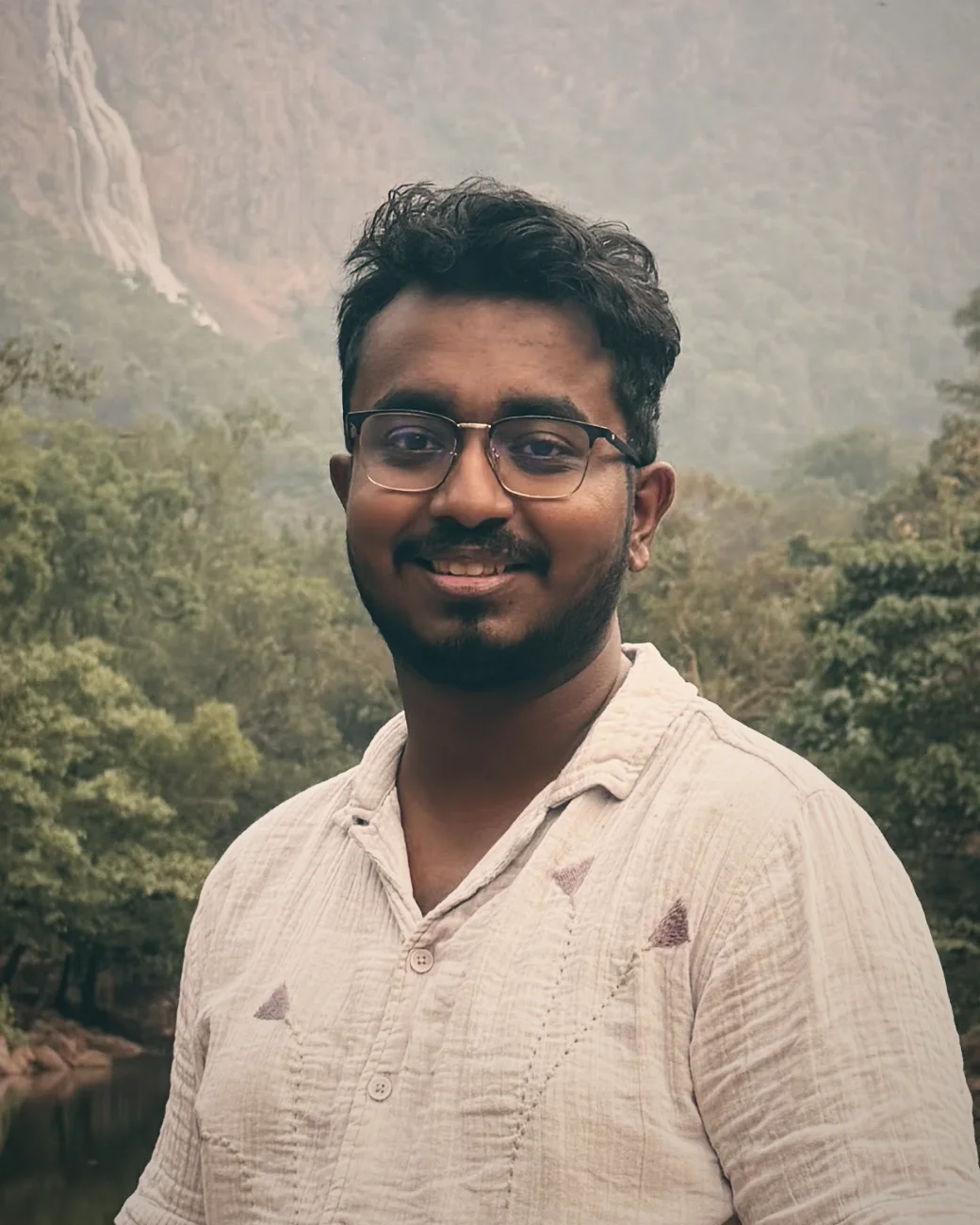 Rownak Mazumder, smiling, in front of a forest waterfall